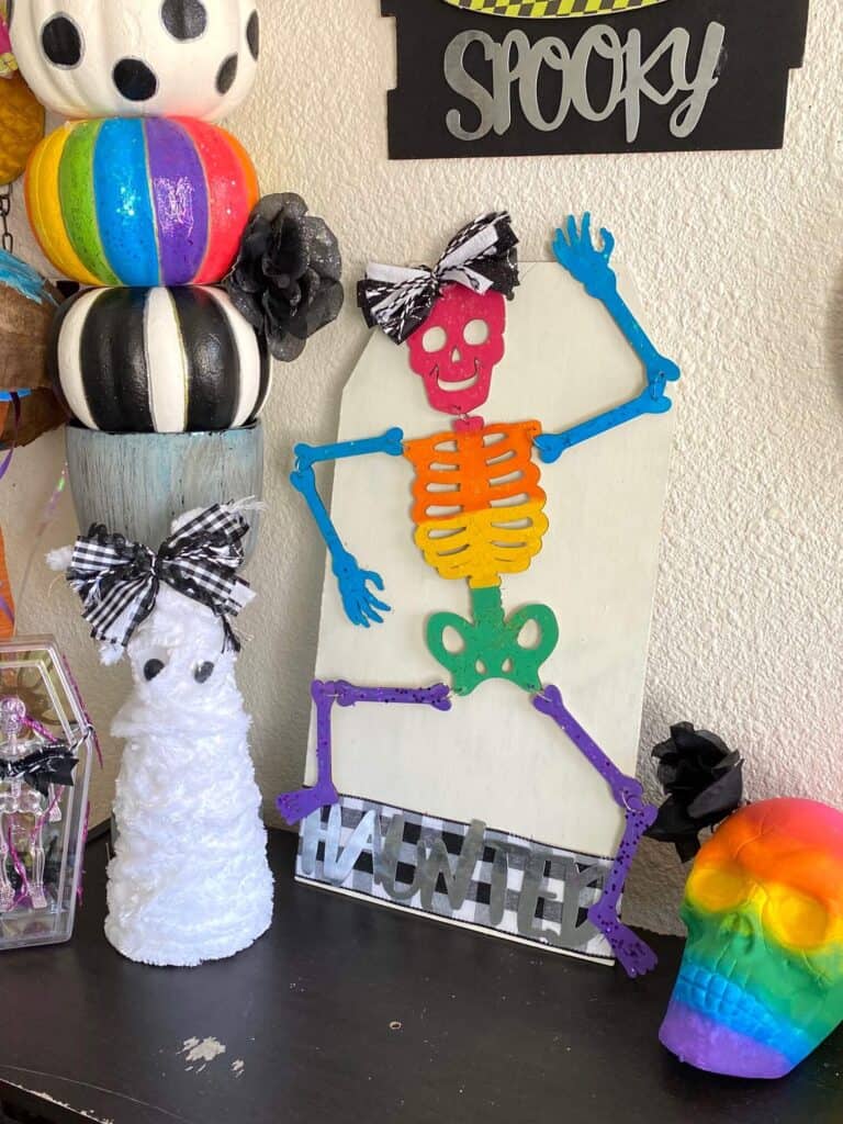 DIY Dollar Tree Rainbow Halloween Skeleton next to a foam cone mummy, a rainbow skull and a pumpkin topiary on a bookshelf.