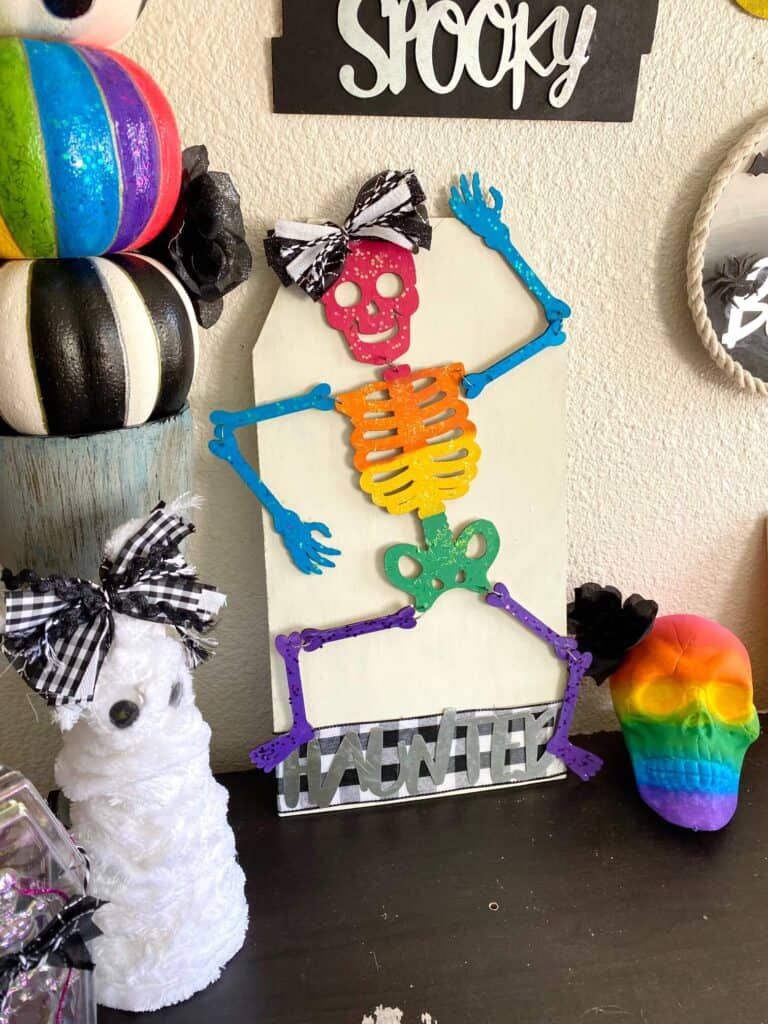 DIY Dollar Tree Rainbow Halloween Skeleton with a haunted sign and a black and white cute bow for your DIY decorations.