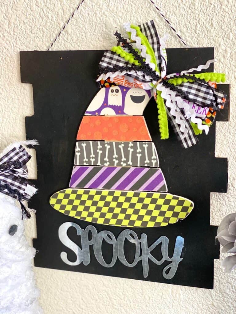 Dollar Tree Spooky Wood Pallet Witch Hat with traditional Halloween colored scrapbook paper, a messy bow at the top, on a black background sign.