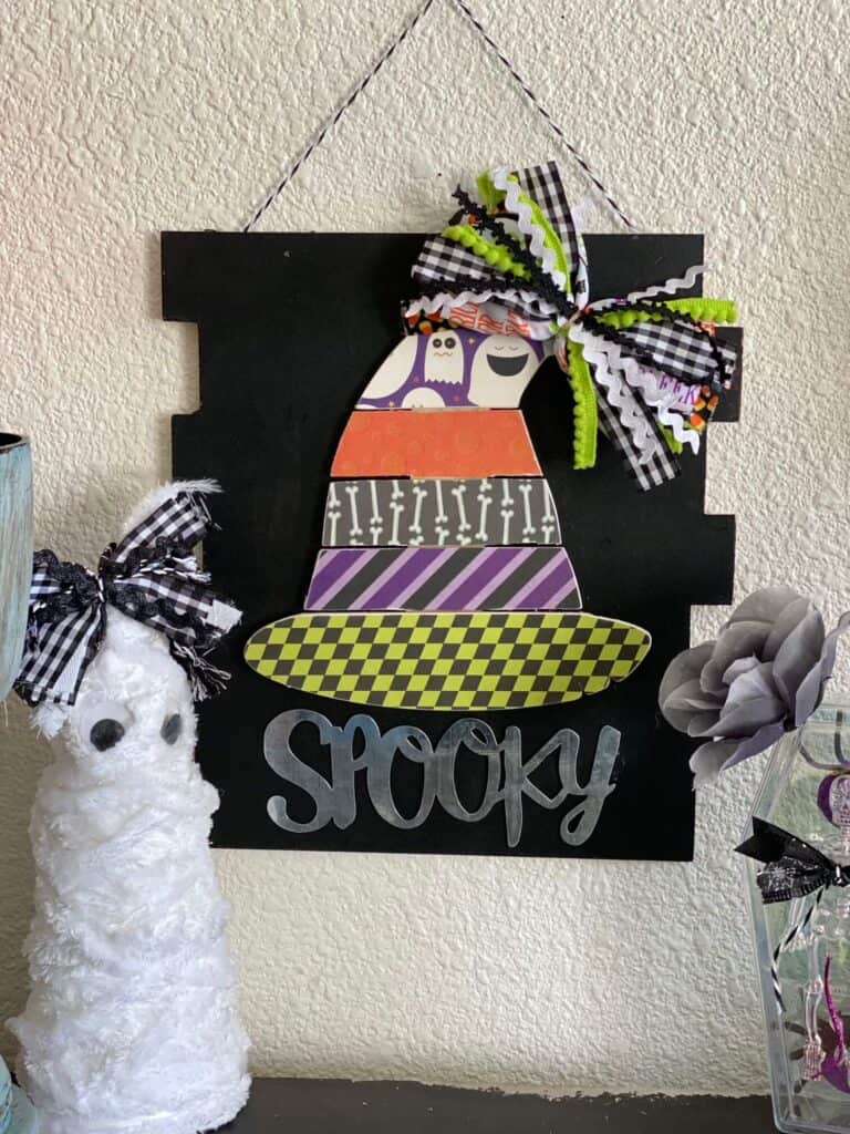 Dollar Tree Spooky Wood Pallet Witch Hat with traditional Halloween colored scrapbook paper, a messy bow at the top, on a black background sign with a foam cone mummy.