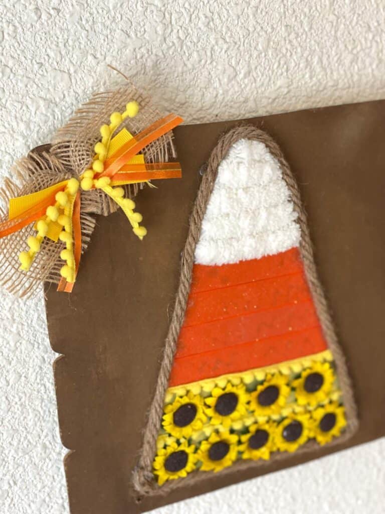 Cute burlap, yellow pom pom trim, and orange and yellow ribbon bow on the top left corner of the candy corn craft.