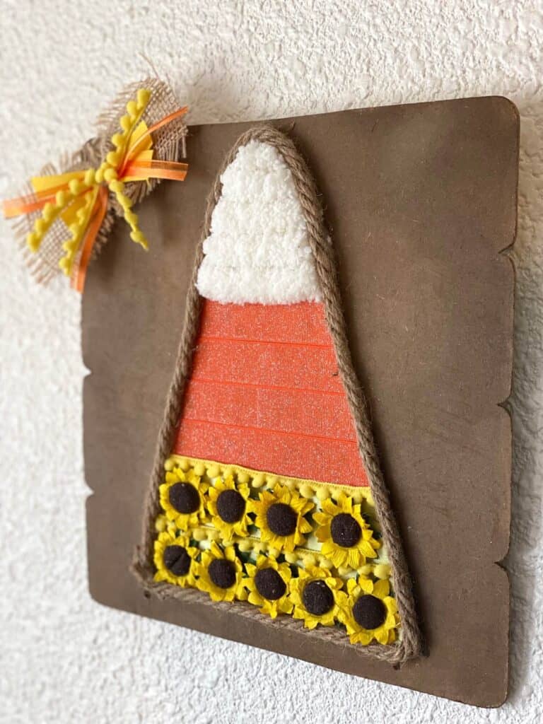 Dollar Tree Mixed Media Candy Corn craft with white chunky yarn, orange ribbon and yellow sunflowers with Jute rope around the edge and a cute bow in the corner.