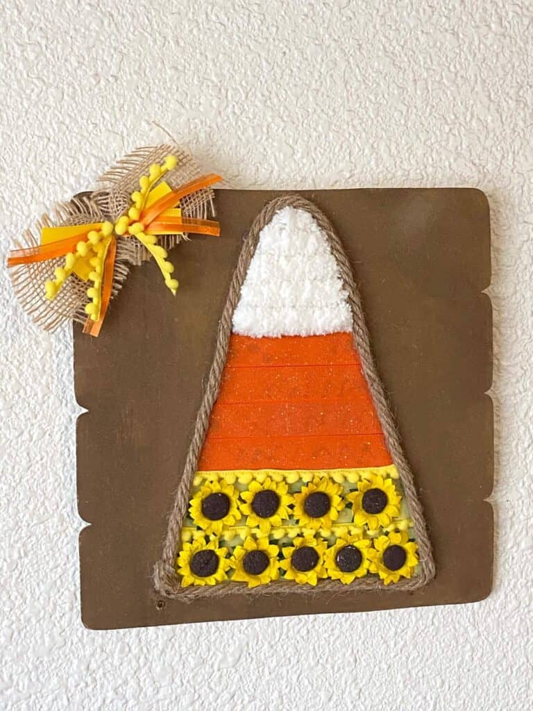 Dollar Tree Mixed Media Candy Corn craft with white chunky yarn, orange ribbon and yellow sunflowers with Jute rope around the edge and a cute bow in the corner.