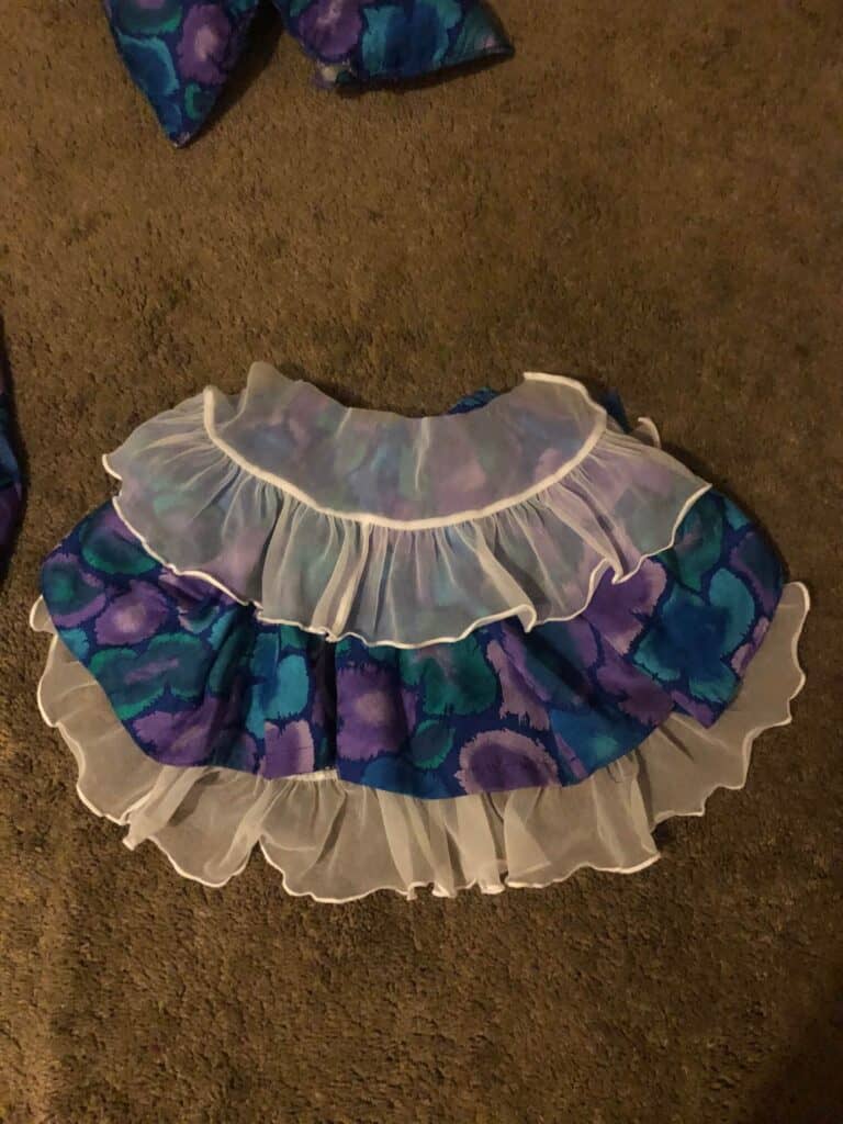 The ruffled lacey fabric along with the blue. purple and green dress fabric layered on the floor together to make a clown collar.