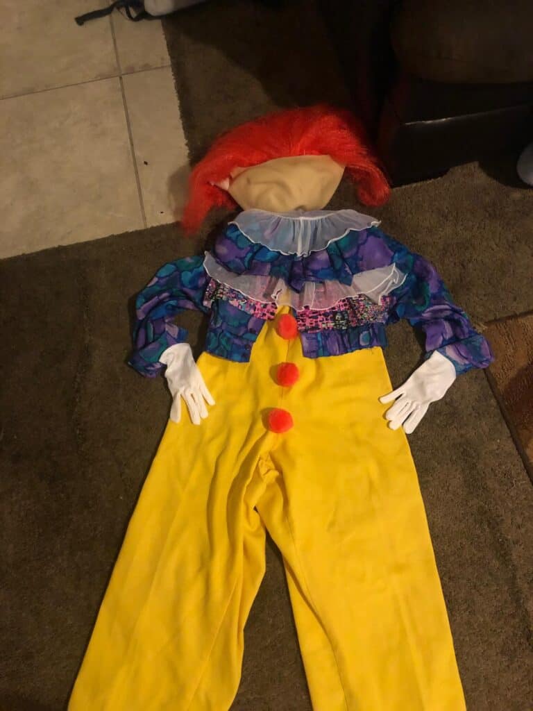 The completed original DIY pennywise the clown costume laid out on the floor with yellow pants, blue and purple top, red wig, and white gloves.