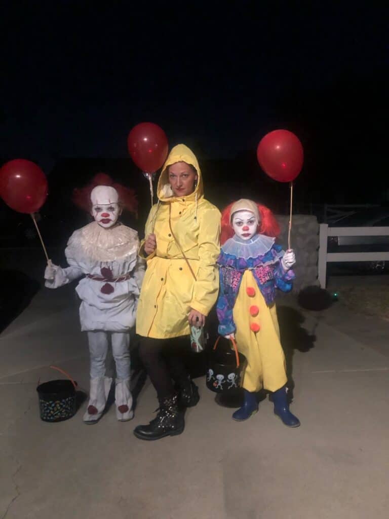 DIY Pennywise the Clown Halloween costumes with the original version of pennywise, the new movie version, and Georgie from the movie IT, all holding red balloons.