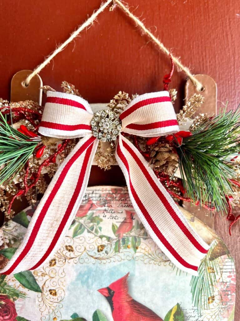 Red and white striped antiqued bow with a Totally Dazzled bling in the center and greenery with red and gold glitter branches.