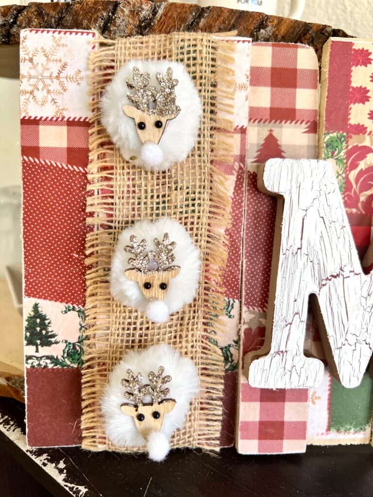 3 white pom pom mini reindeer glued to the strip of burlap on the left hand side of the Merry sign.