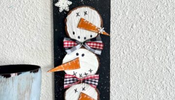Wooden stacked snowmen decor made with wood round and 4 snowmen faces stacked on top of eachother with bows in between on a black snowy background with a few snowflakes to decorate for winter.