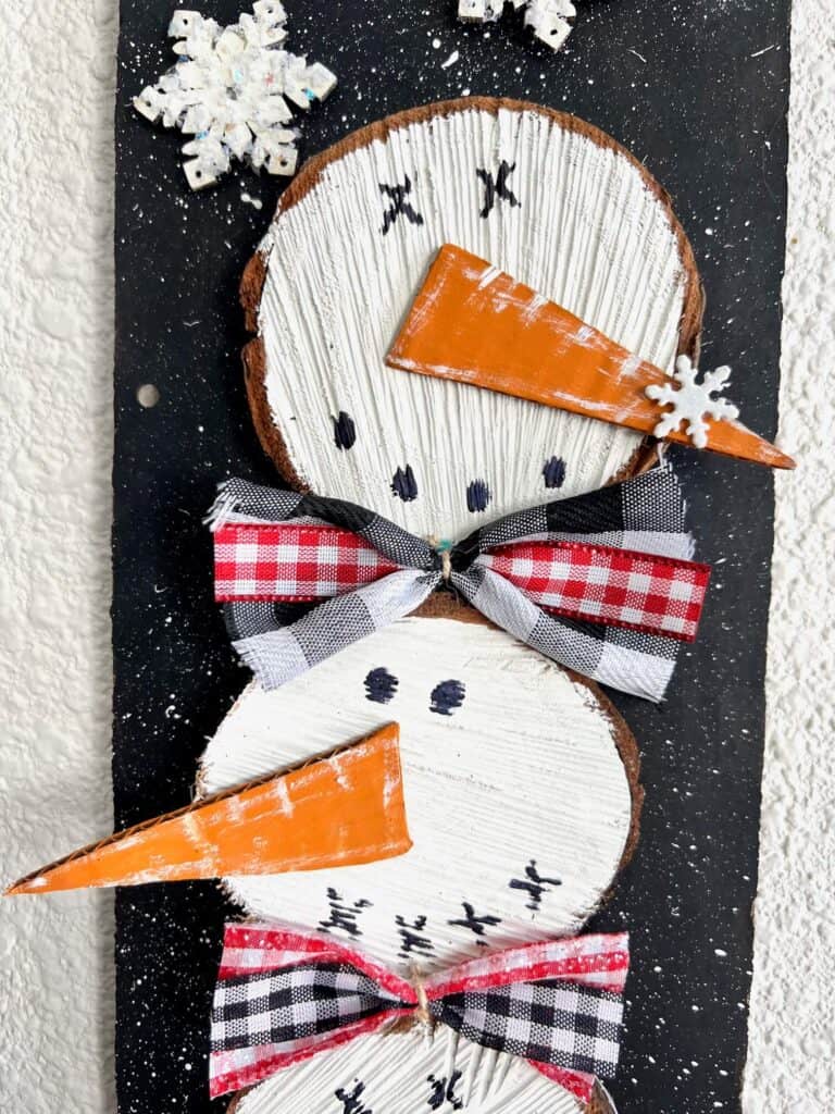 Close up of the Wooden round snowmen faces with a big orange carrot nose and bow ties.
