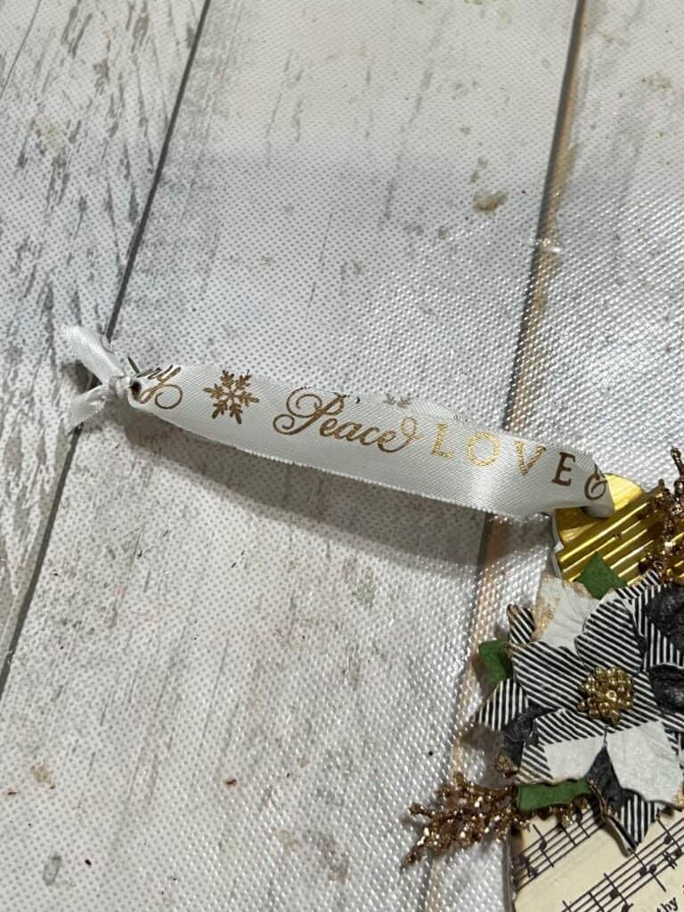 White ribbon with gold words "peace love and joy" as the ornament hanger.