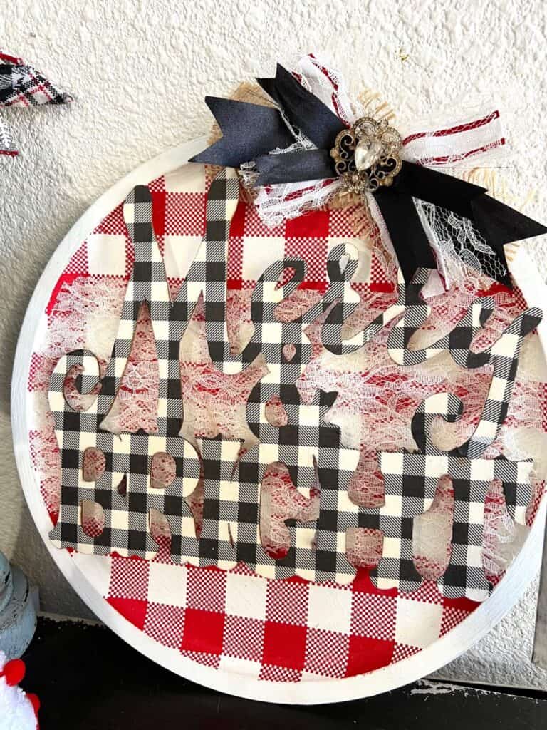 Dollar Tree Merry and Bright Christmas Pizza Pan Door Hanger Wreath with red and white check background and buffalo check wooden word cutout and a messy bow with vintage bling.