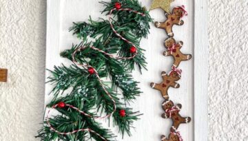 Dollar Tree Gingerbread Men DIY wall hanging decor made with mini gingies stacked on top of each other helping to put the gold star on top of the Christmas Tree made with wired faux pine, red bells, and bakers twine garland and faux snow underneath with a 2 candy canes in the shape of a heart.