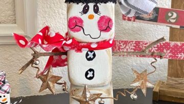 Dollar Tree Foam Dice Snowman DIY christmas and winter decor with a black and white striped hat, red polka dot scarf, sticks for arms, holding a jingle bell garland with rusty stars for decoration.