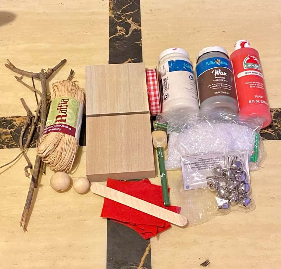 Supplies needed to make a santa and reindeer with wood blocks, sticks, felt, paint, faux snow, jingle bells, adn wood beads.