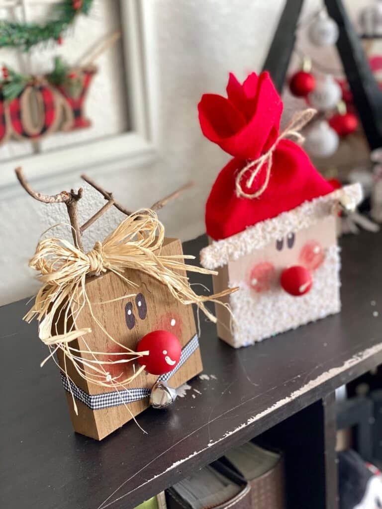 Wood block santa and rudolph the red-nosed reindeer made with 4x4 blocks, painted whimsy faces, wood bead red noses, raffia bow, and faux snowy glitter beard and jingle bells.