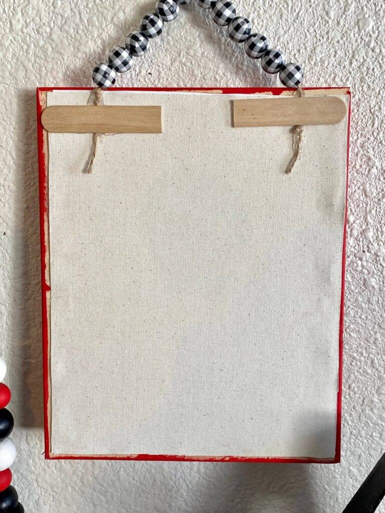 Back of the completed reverse canvas with eh Twine wood bead hanger glued to the back and popsicle sticks reinforcing.