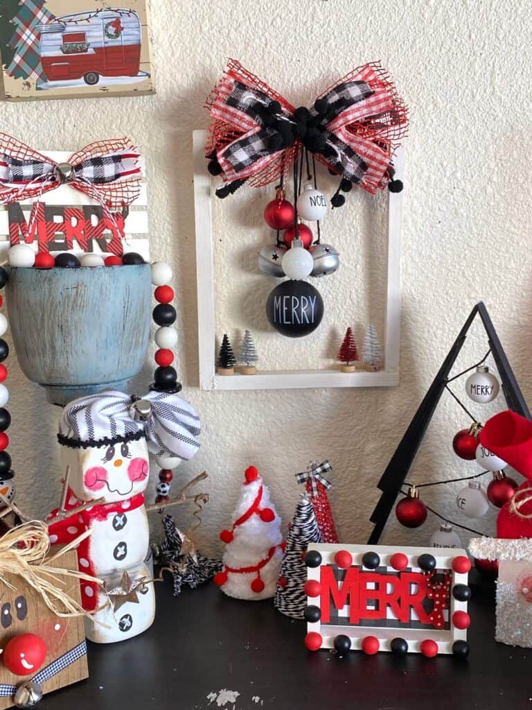 A whole bunch of DIY red black and white christmas decorations on a bookshelf staged with the completed hanging ornament reverse canvas.