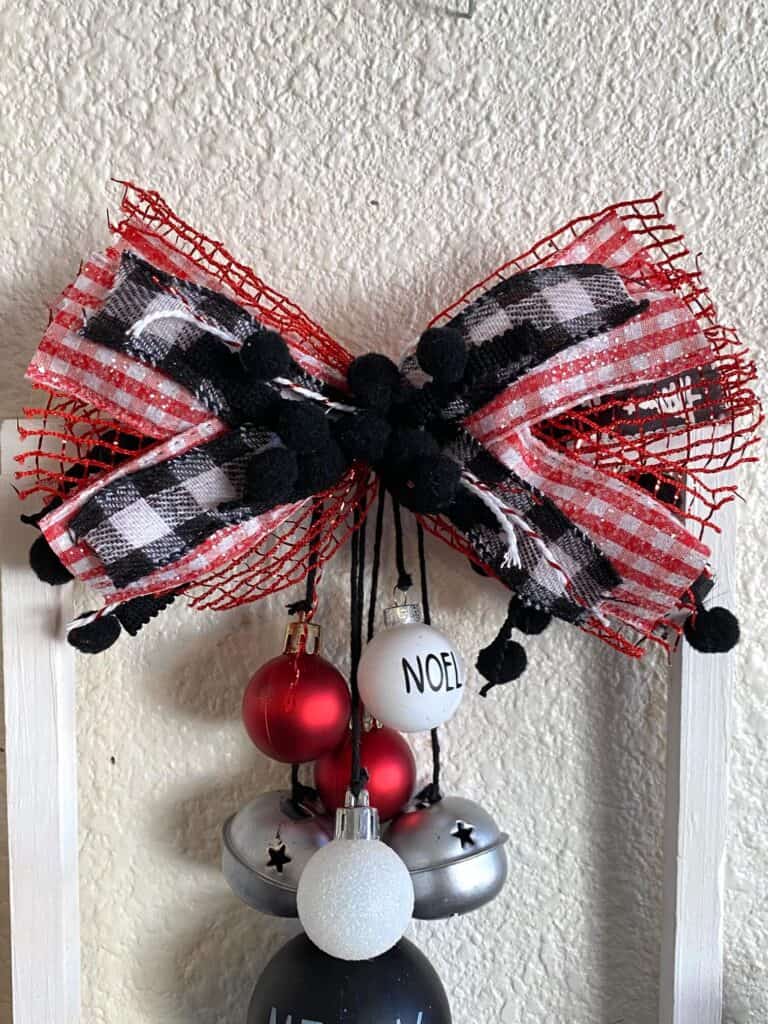 A big messy bow with red and white check ribbon and black pom pom trim at the top of the project.