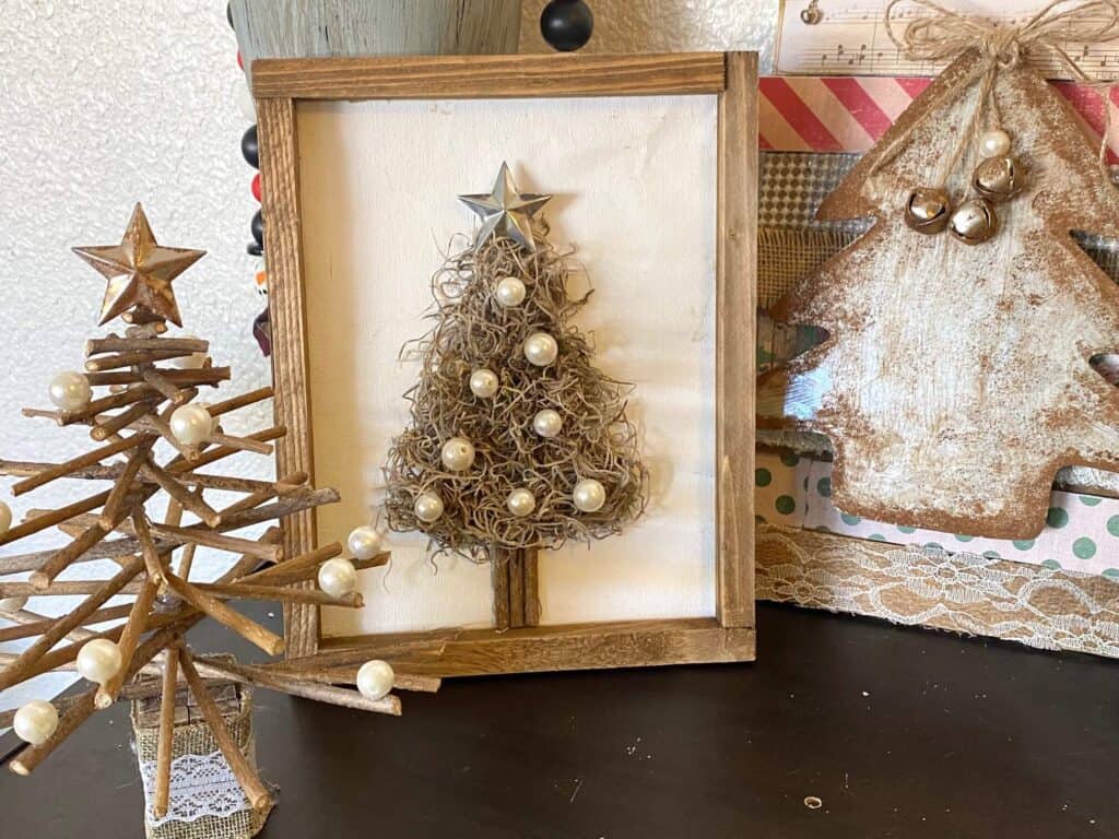 The spanish moss Christmas Tree staged on a bookcase with a Stick Christmas tree and a faux rust christmas tree decor.