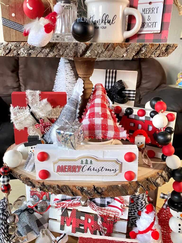 Middle tier of the wooden tray with wood block presents, snowman wood bead garland, Merry shelf sitter, and red and black stuffed Christmas tree.
