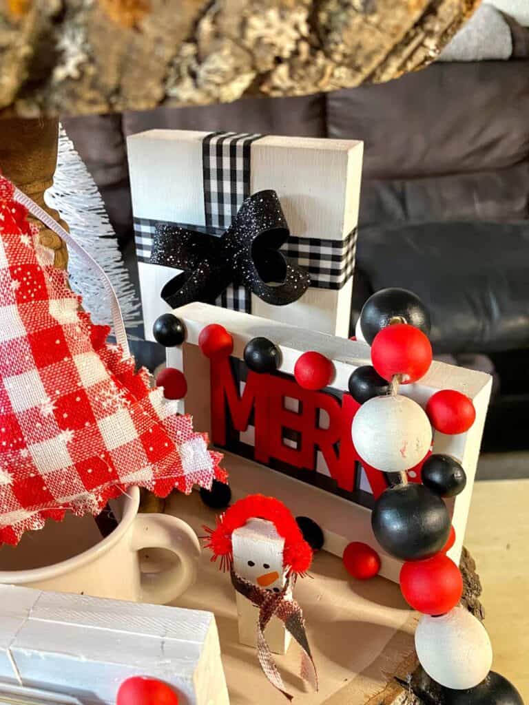 Close up of the Merry tiered tray sitter with black and white buffalo check and the word "merry" in red, next to a Jenga Block snowman.