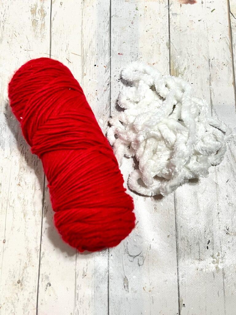A roll of red yarn and white chunky yarn sitting together on a table.