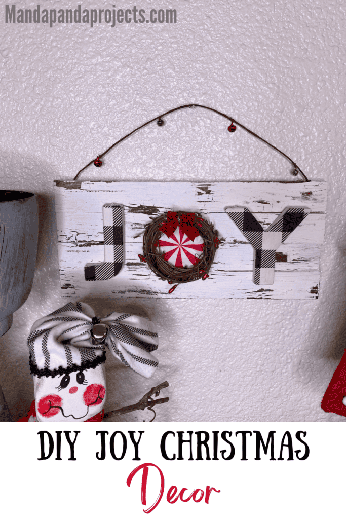 DIY JOY Christmas Sign on a white distressed chippy background with the O as a grapevine wreath with a peppermint napkin inside and a berry wired garland hanger.
