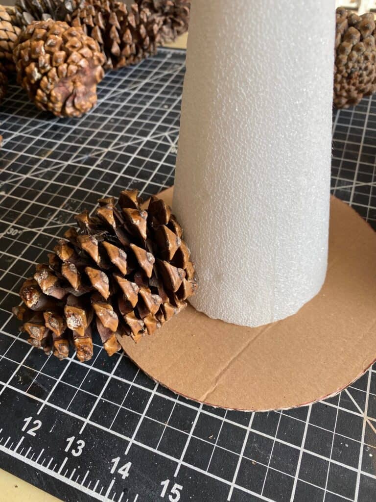 A foam cone glued to a circle cardboard base with one pine cone glued to the bottom left.