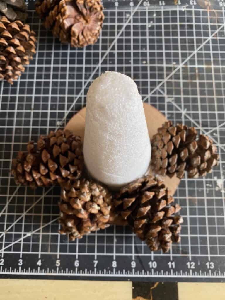 A foam cone glued to a circle cardboard base with 4 pine cones glued around the bottom.
