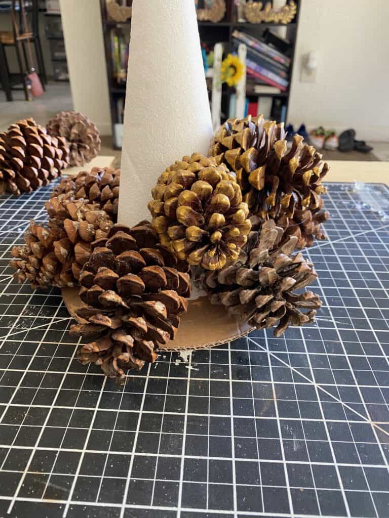 A foam cone glued to a circle cardboard base with pine cones glued all around the cone from the bottom up.