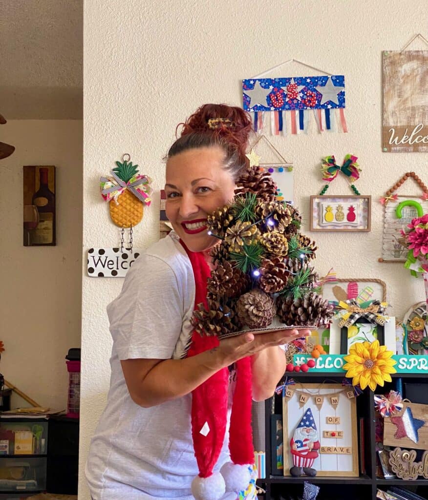 Amanda holding the completed pine cone christmas tree wearing a red santa scarf .