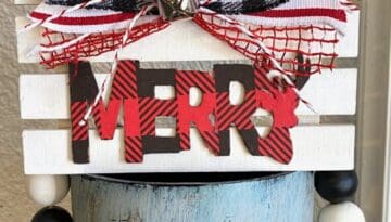 Tiered Tray Merry Pallet Board with a red and black buffalo check word Merry and a cute bow and silver bell to decorate for christmas.