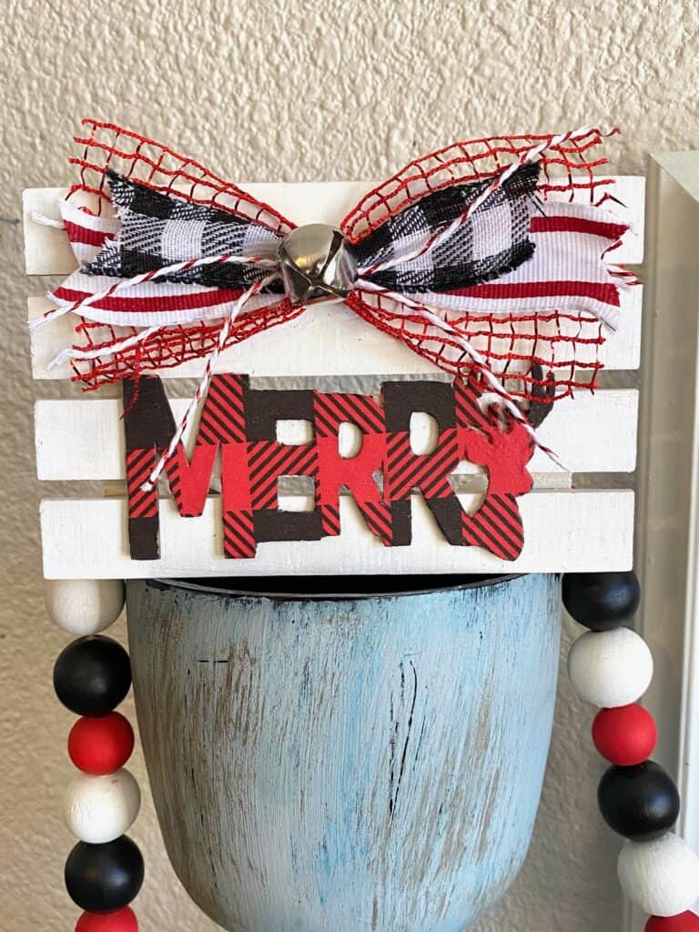 Tiered Tray Merry Pallet Board with a red and black buffalo check word Merry and a cute bow and silver bell to decorate  for christmas.