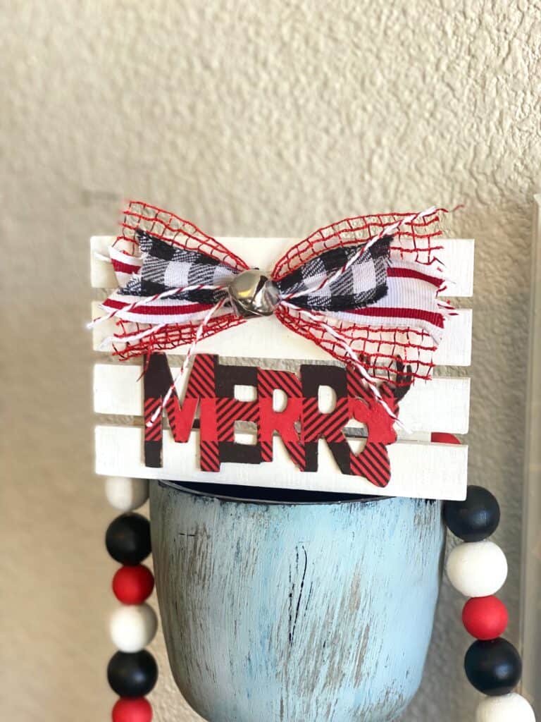 Tiered Tray Merry Pallet Board with a red and black buffalo check word Merry and a cute bow and silver bell to decorate  for christmas.