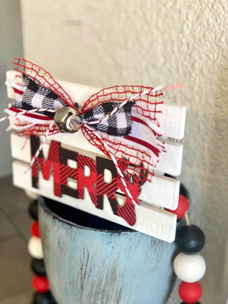 Tiered Tray Merry Pallet Board with a red and black buffalo check word Merry and a cute bow and silver bell to decorate  for christmas.