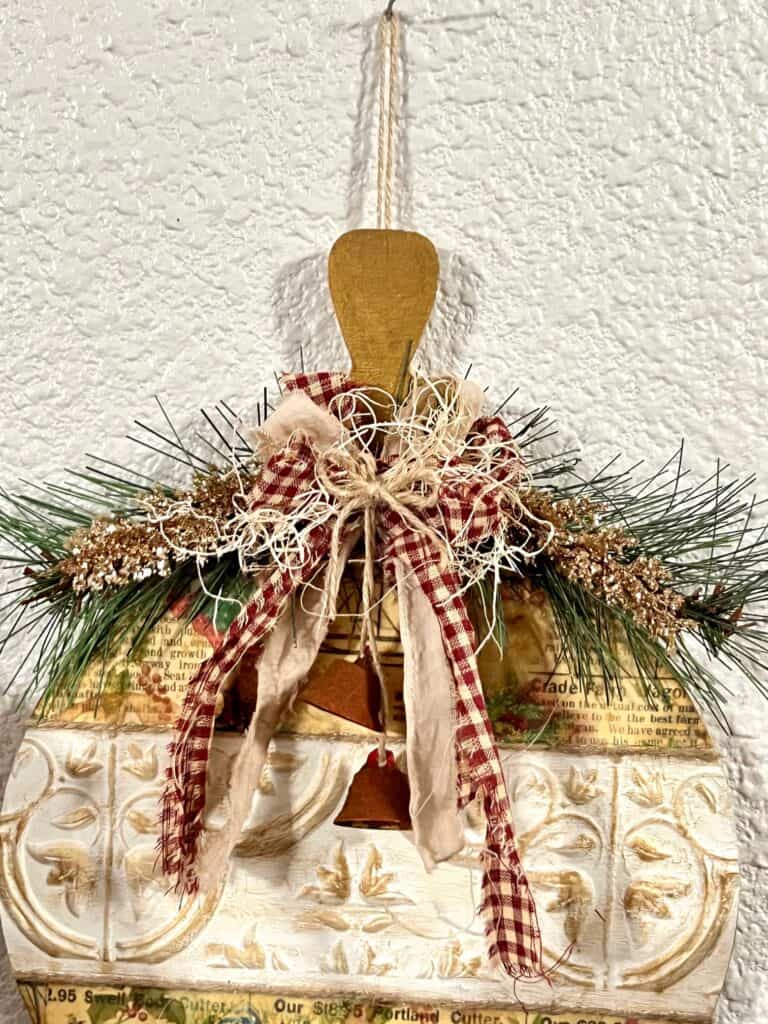 Faux greenery, gold glitter branches, and a fabric bow at the top of the wooden ornament.