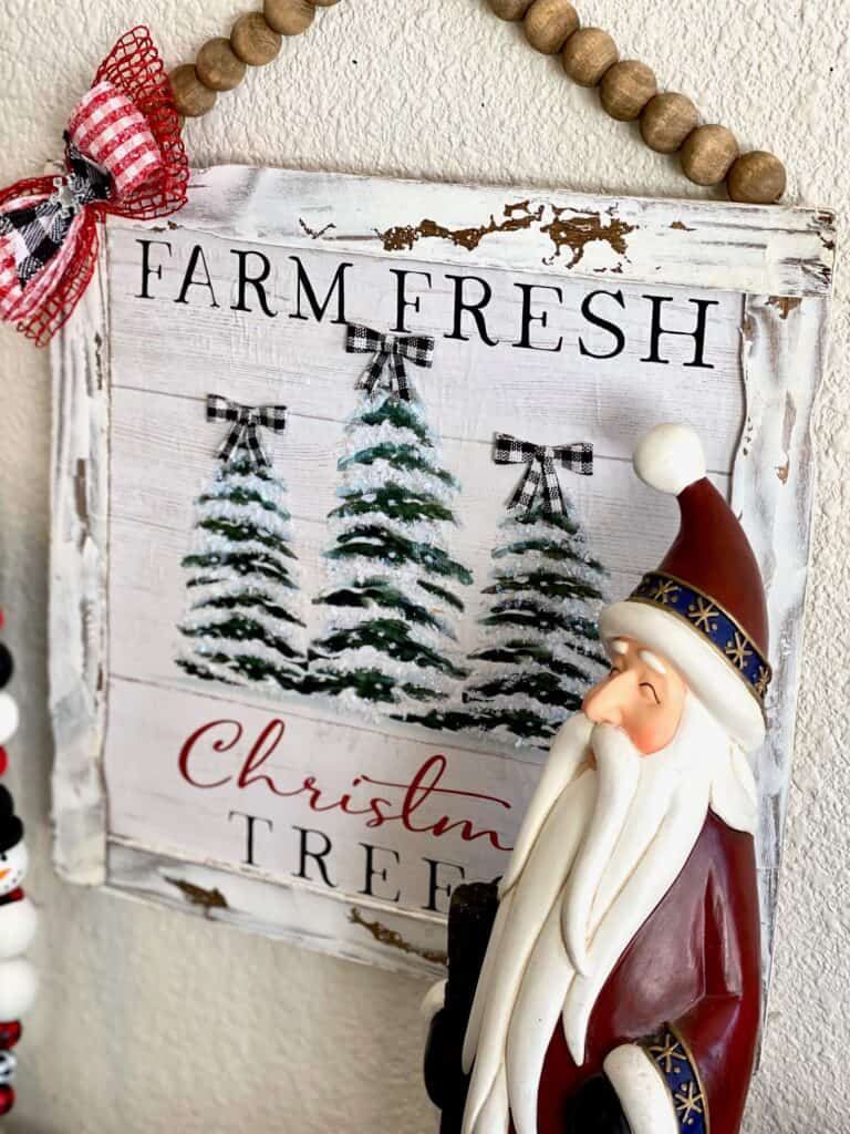 The Christmas tree frame hanging on the wall next to a tall santa.