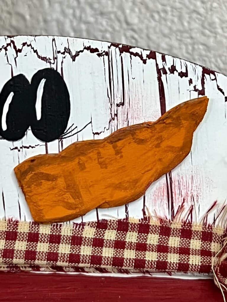 Cardboard carrot nose with brown antique wax lines.
