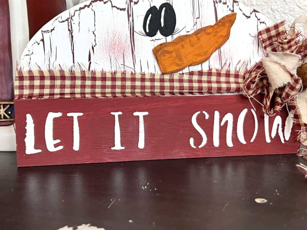 The phrase "let it snow" stenciled across the bottom center of the snowman.