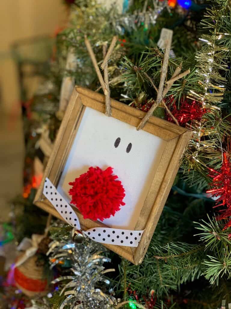 Rudolph the red nosed reindeer reverse canvas hanging on a christmas tree.