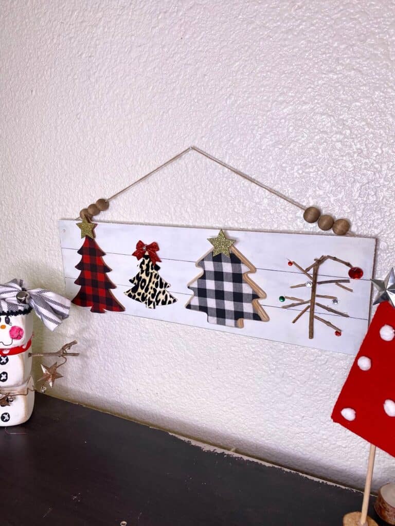 The completed Christmas Tree decor project hanging on the wall with a Snowman to the left and yarn wrapped standing Christmas trees to the right.