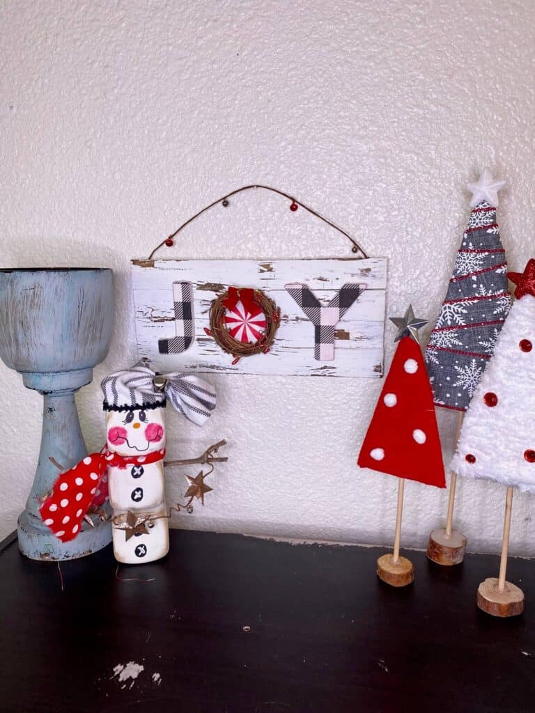 The DIY Christmas JOYT sign hanging on the wall next to other DIY christmas decor on a bookshelf. 