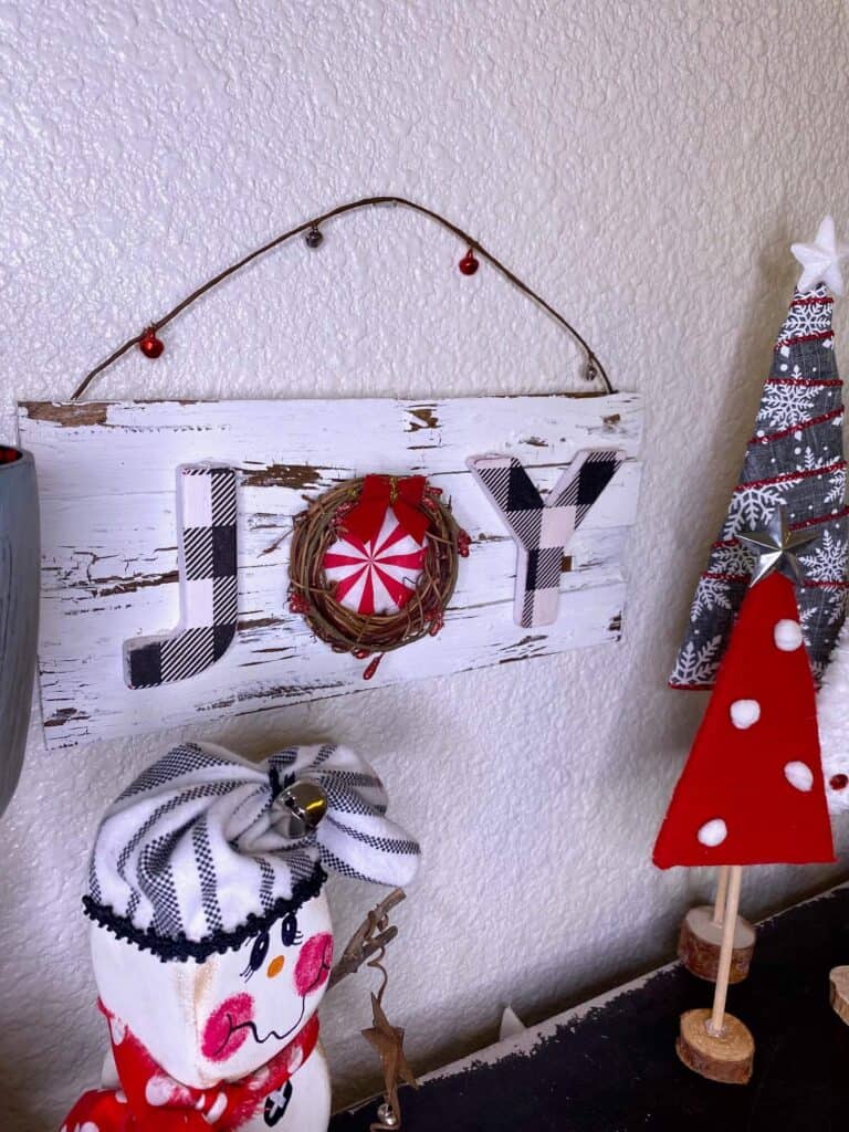 A foam dice snowman and cardboard christmas trees sitting on a bookshelf staged with the JOY sign on wooden shims.