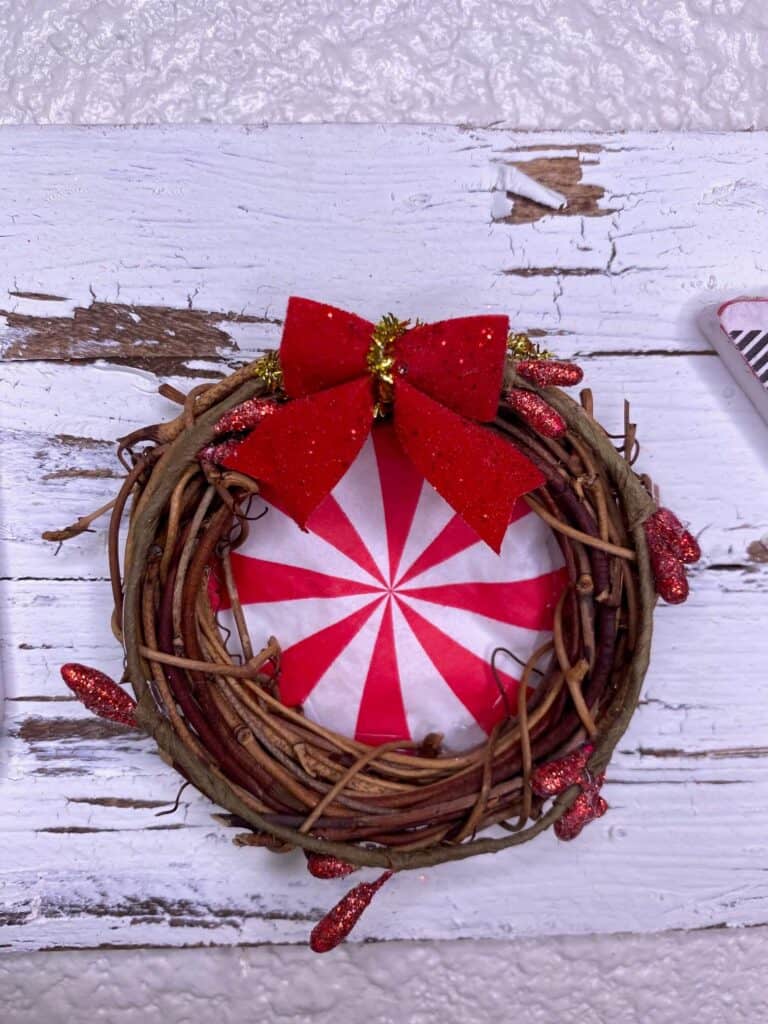 the O grapevine wreath with a peppermint in the center, sparkly berry garland, and a red glitter bow on the top.