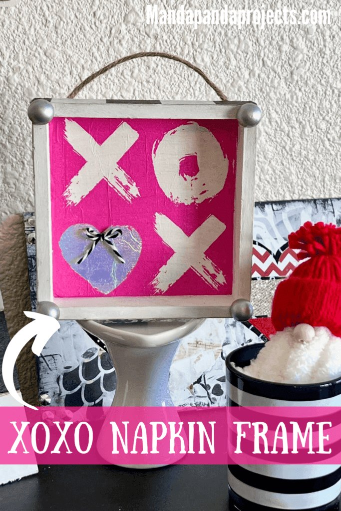 XOXO Valentines Day Napkin Shelf Sitter with a hot pink XOXO napkin that the second O is a silver heart, with a silver half wood bead on each corner and black and whit buffalo check print on each of the 4 sides of the box.