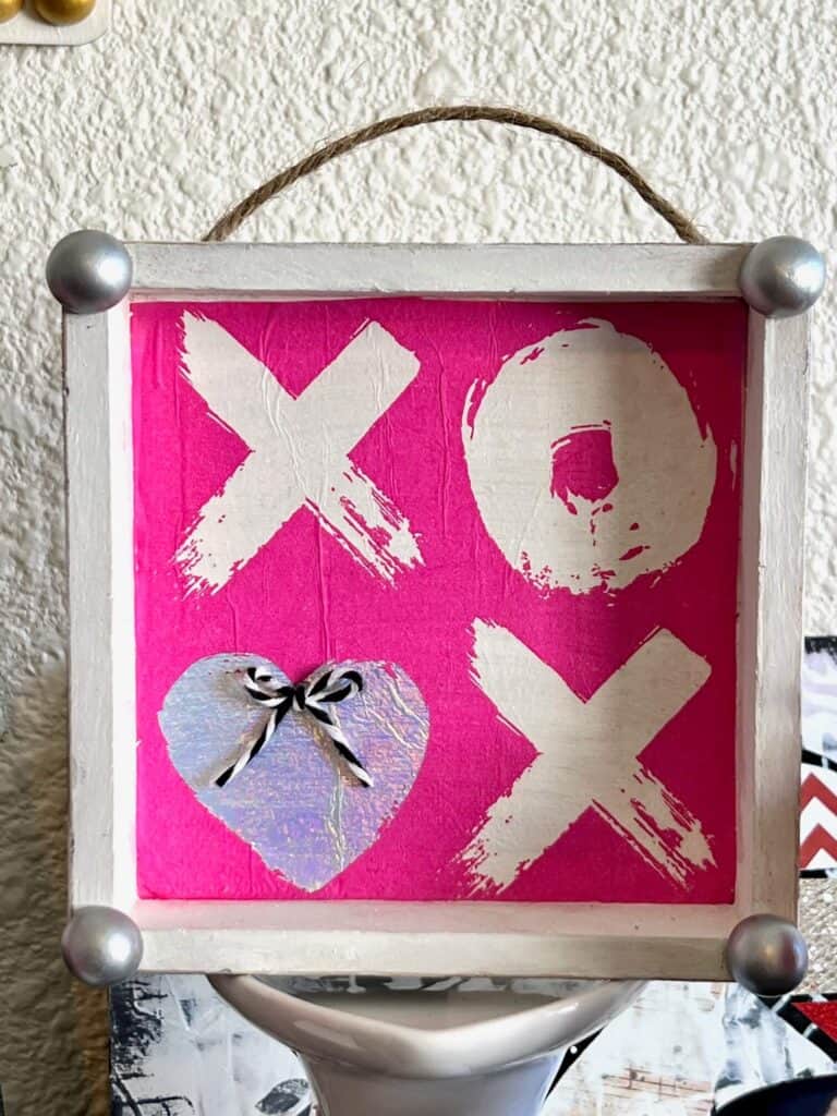 Close up of the front of the box frame with a hot pink XOXO napkin that the second O is a silver heart with a small bow.