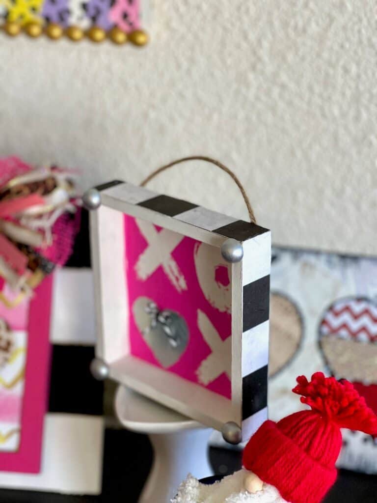 XOXO Valentines Day Napkin Shelf Sitter with a hot pink XOXO napkin that the second O is a silver heart, with a silver half wood bead on each corner and black and whit buffalo check print on each of the 4 sides of the box.