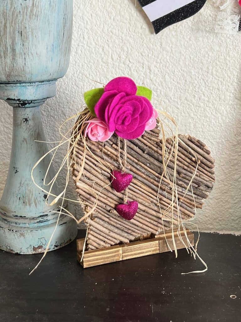 Rustic Valentines Day Stick Heart DIY Decor with felt roses and hanging pink sparkly hearts and raffia.