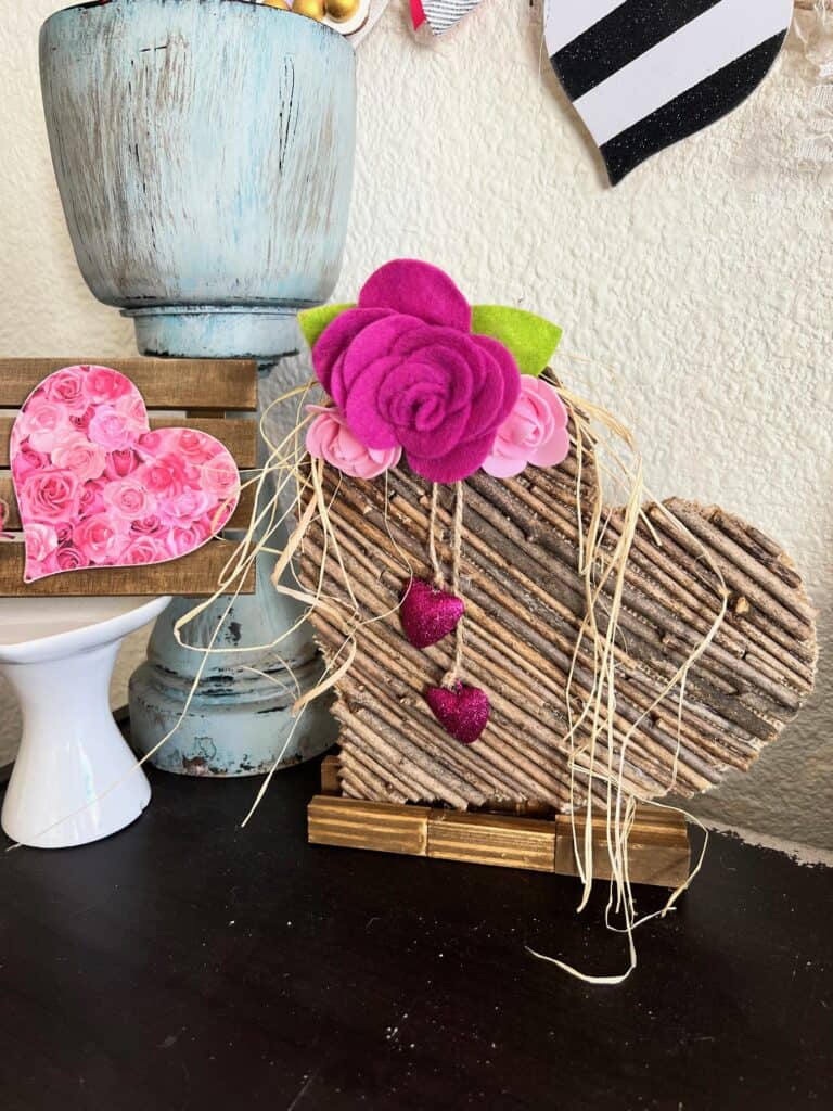 Rustic Valentines Day Stick Heart DIY Decor with felt roses and hanging pink sparkly hearts and raffia.